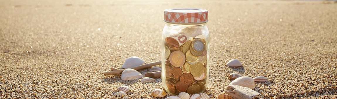 Pot en verre posé sur le sable et rempli de pièces de monnaie